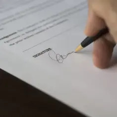 Dłoń podpisująca dokument długopisem.